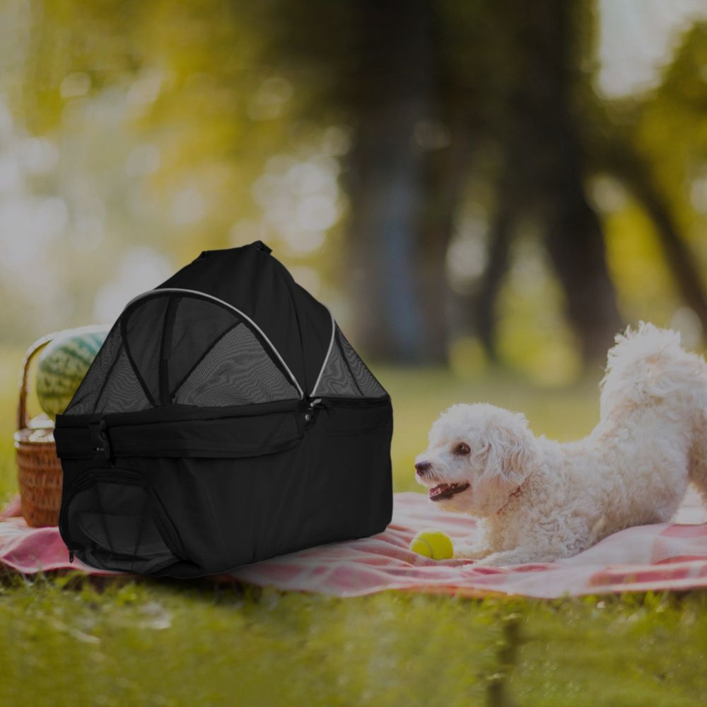 Small white dog on a picnic blanket beside a black pet travel stroller in a sunny park – Pet &amp; Travel Adventure collection image