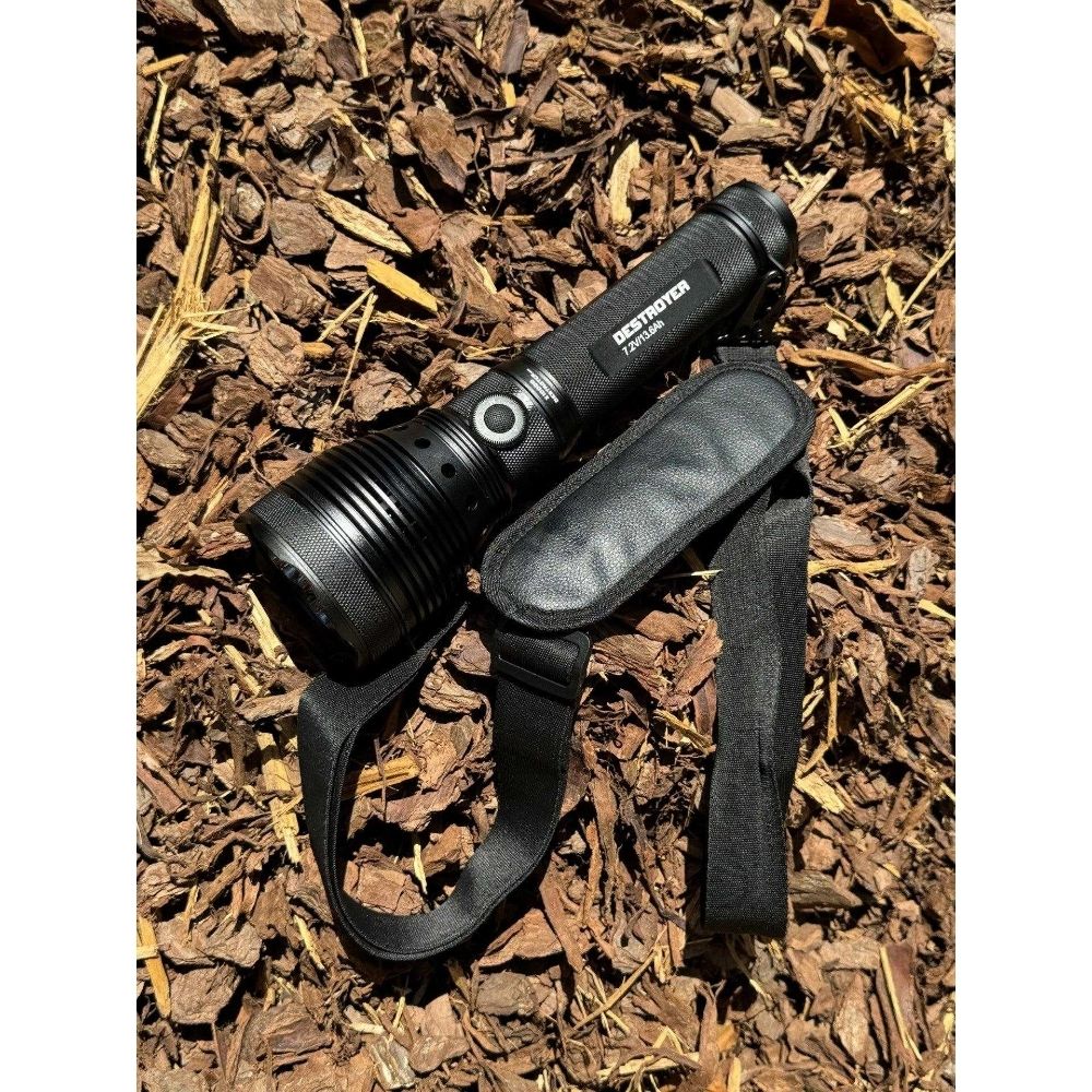 Powertac X10000 Destroyer flashlight with padded shoulder strap lying on wood chips outdoors