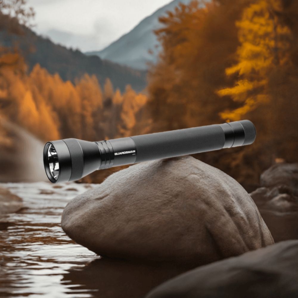 Powertac Guardsman long flashlight resting on a river rock with blurred autumn mountain scenery
