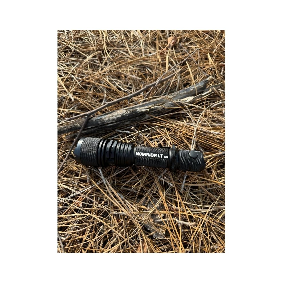 Powertac Warrior LT G5 tactical flashlight lying on dry pine needles in the woods.