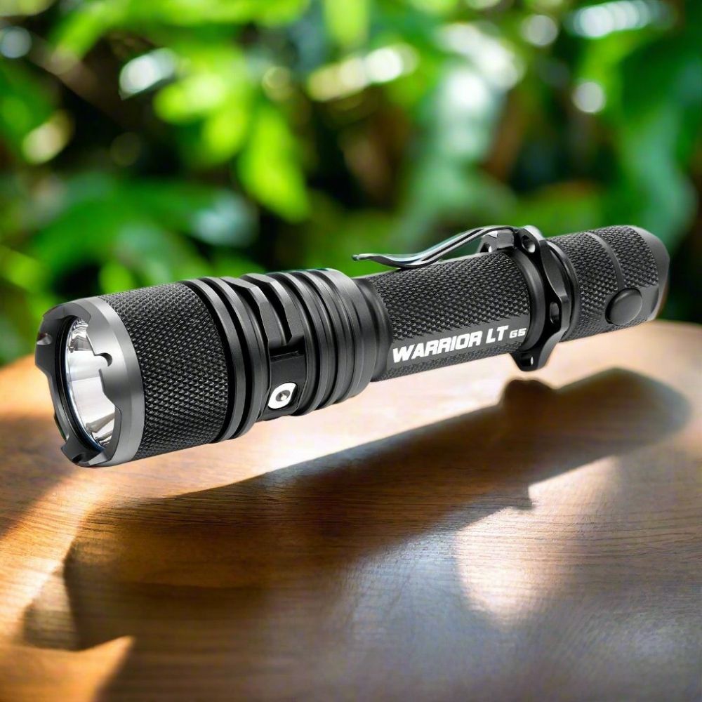 Powertac Warrior LT G5 compact tactical flashlight on a wooden tabletop with lush green foliage in the background.