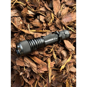 Powertac Warrior LT G5 flashlight resting on rugged bark mulch for an outdoor adventure scene.