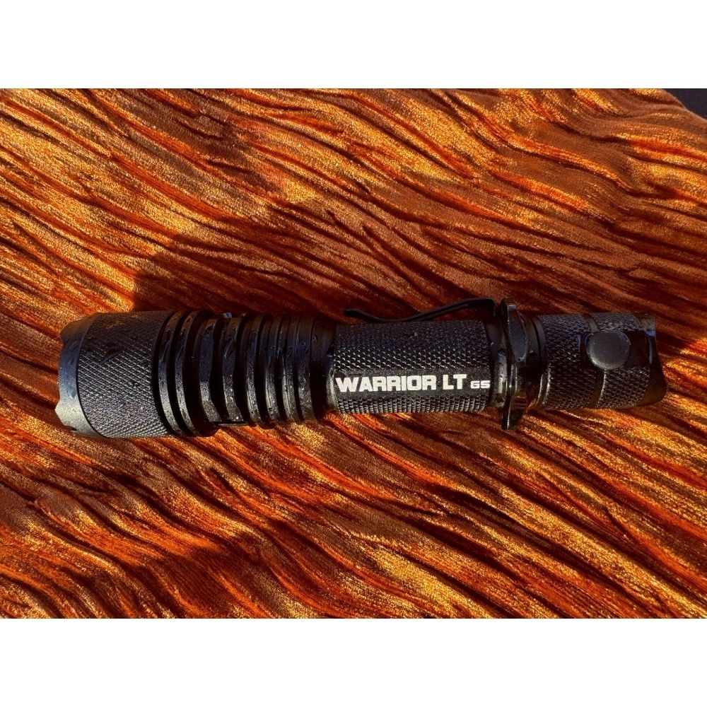 Powertac Warrior LT G5 flashlight with water droplets lying on textured orange fabric.