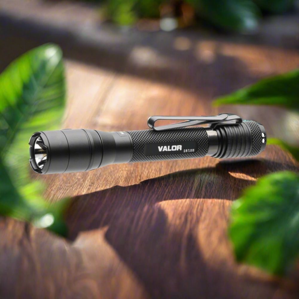 Powertac Valor AA tactical flashlight on wooden table with soft green foliage in background