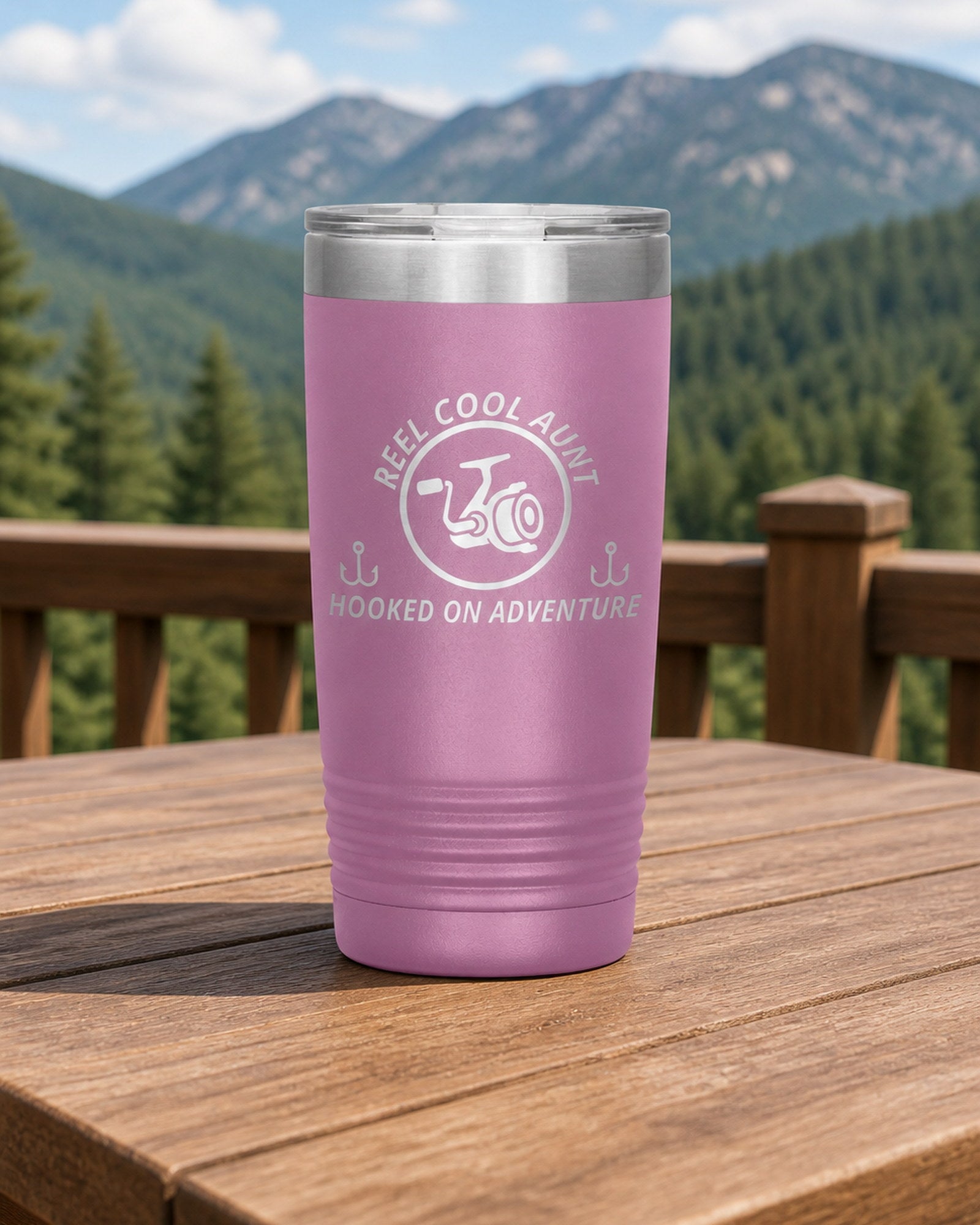 Light Purple 20-ounce REEL COOL AUNT engraved tumbler on a sturdy cabin porch table overlooking forested mountains.