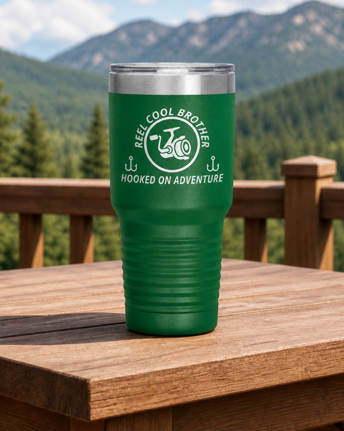 Green 30-ounce REEL COOL BROTHER engraved tumbler on a sturdy cabin porch table overlooking forested mountains.