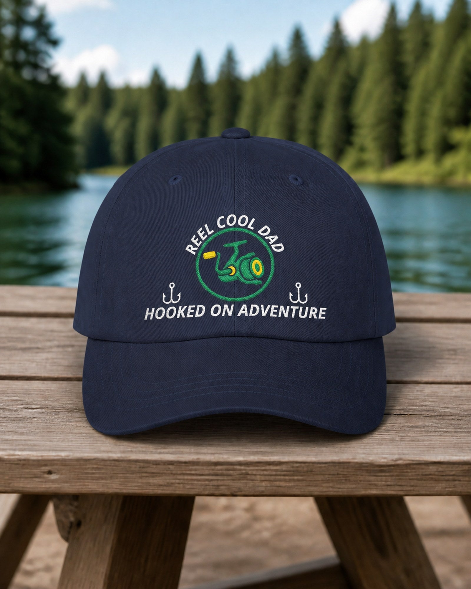 Navy REEL COOL DAD embroidered dad cap on a weathered wooden picnic table beside a pine-lined forest lake.