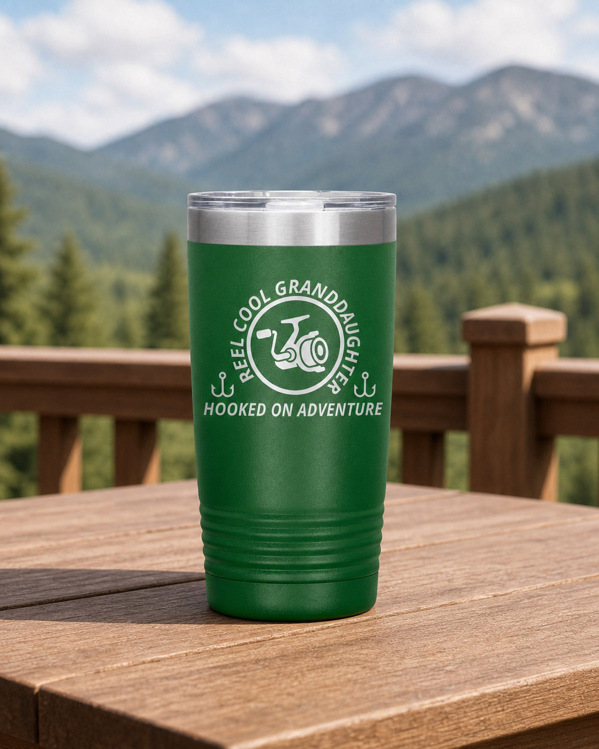 Green 20-ounce REEL COOL GRANDDAUGHTER engraved tumbler on a sturdy cabin porch table overlooking forested mountains.