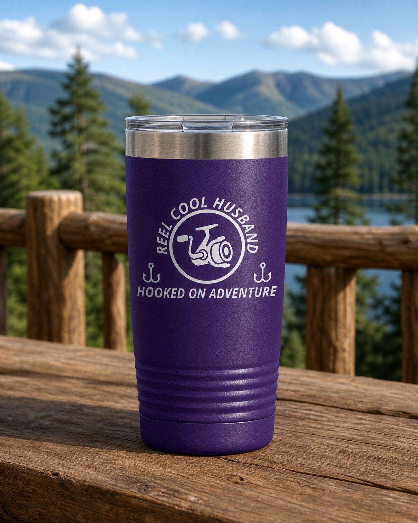 Purple 20-ounce REEL COOL HUSBAND engraved tumbler on a sturdy cabin porch table overlooking forested mountains.