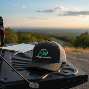 REEL COOL HUSBAND trucker cap with black front and charcoal mesh back displayed on a scenic outdoor tailgate.