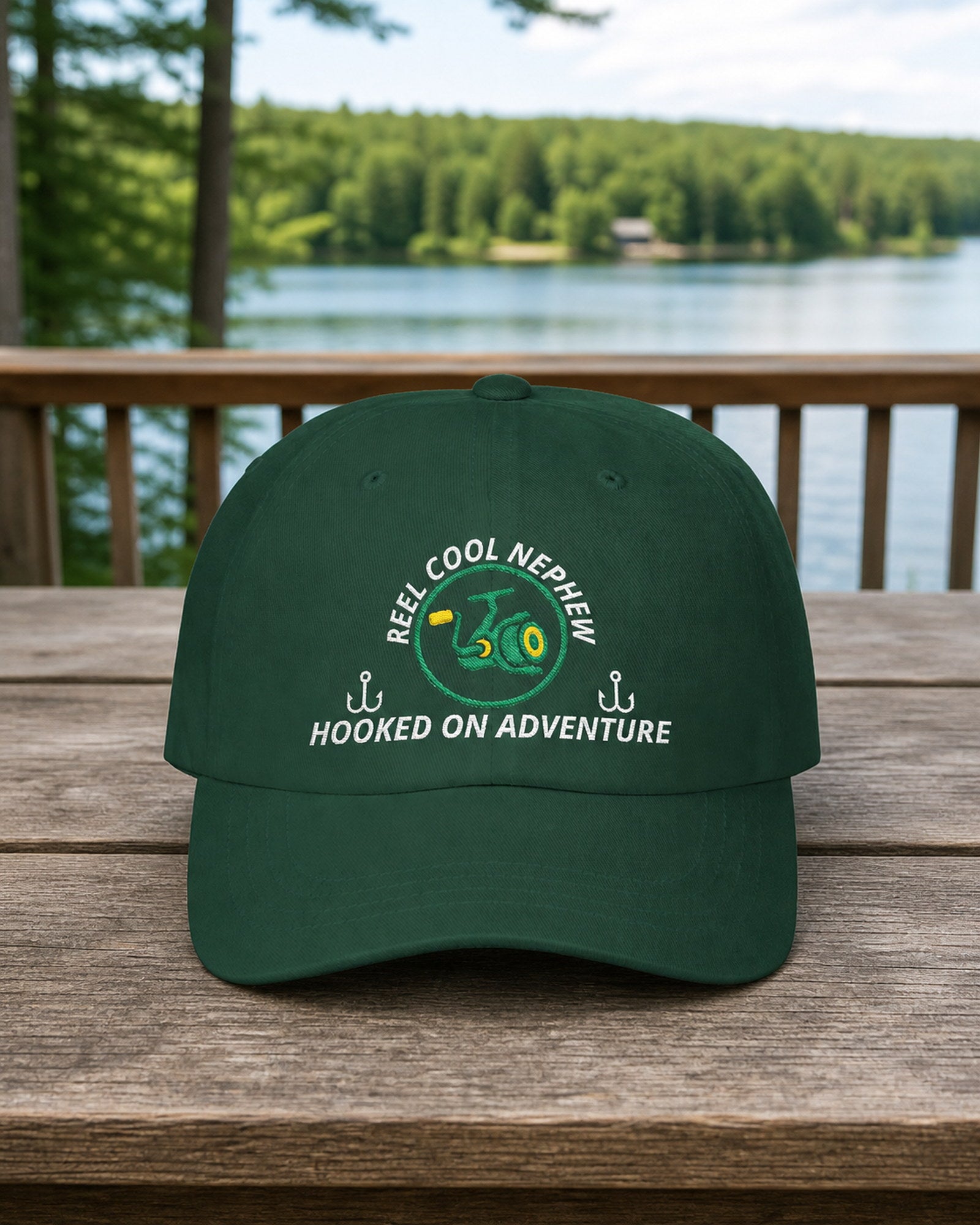 Spruce REEL COOL NEPHEW embroidered dad cap on a full-size cedar cabin porch table overlooking a forest lake.