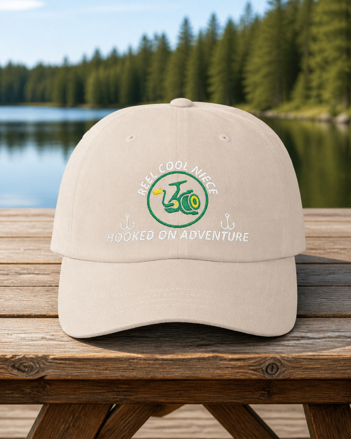 Stone REEL COOL NIECE embroidered dad cap on a weathered wooden picnic table beside a pine-lined forest lake.