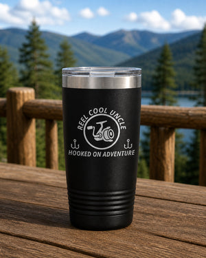 Black 20-ounce REEL COOL UNCLE engraved tumbler on a sturdy cabin porch table overlooking forested mountains.